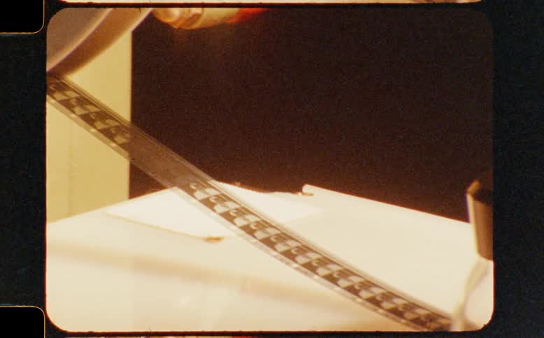 A nostalgic pan across vintage 8mm film editing equipment, from a spinning reel to a viewer loupe resting on the filmstrip