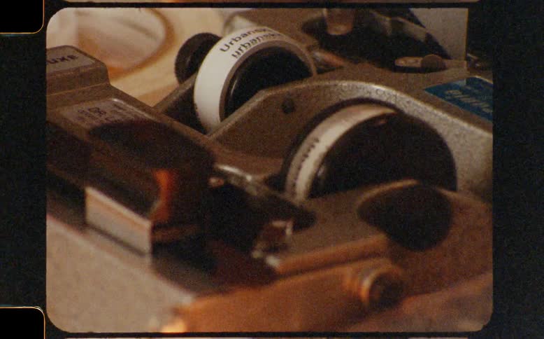 Macro shot of a vintage film splicer's mechanical rollers spinning with authentic film grain and light leaks