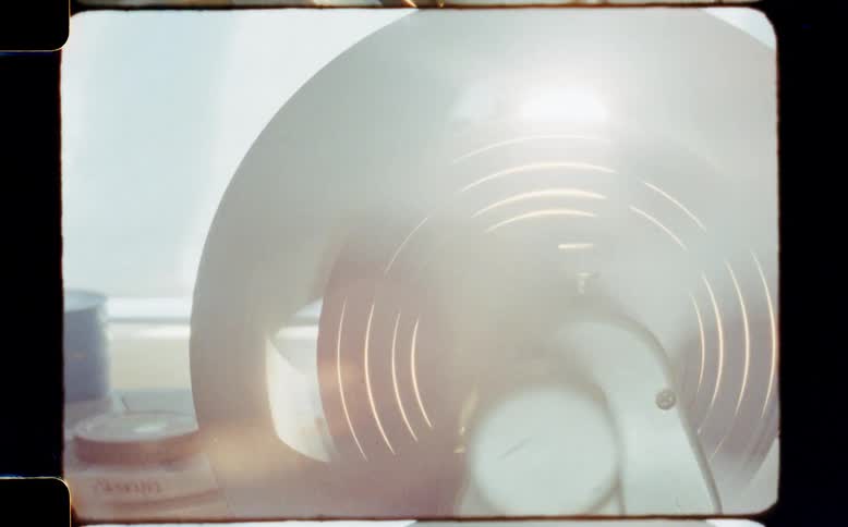 A hand manually cranks a vintage film rewinder, causing the reel to spin with hypnotic motion blur and light reflections