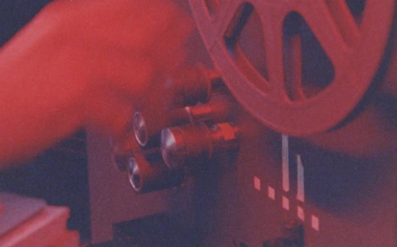 A stylized montage of grainy, vintage-style footage shows a hand operating a film reel on an old projector