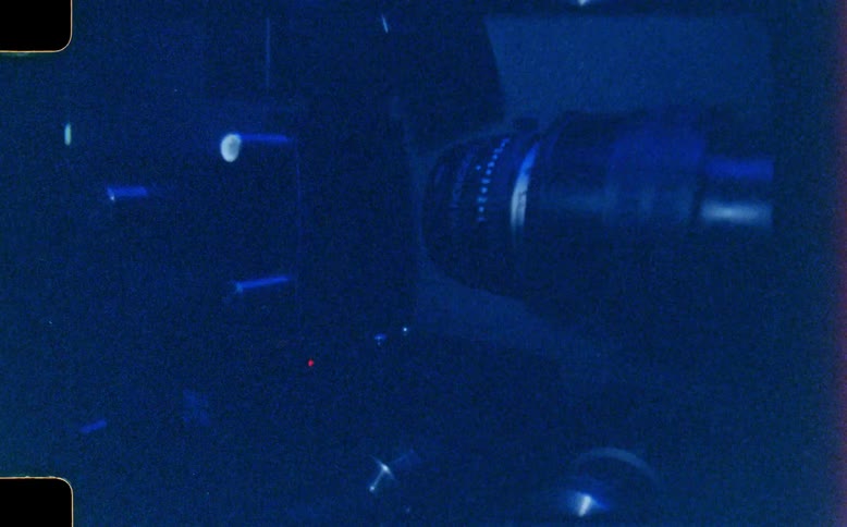 Vintage Super 8mm film captures a close-up of a projector's lens and flickering lamp with authentic grain, sprocket holes, and light leaks