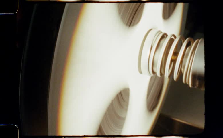 A close-up of a vintage film reel spinning rapidly on a projector, with authentic film grain and sprocket holes visible