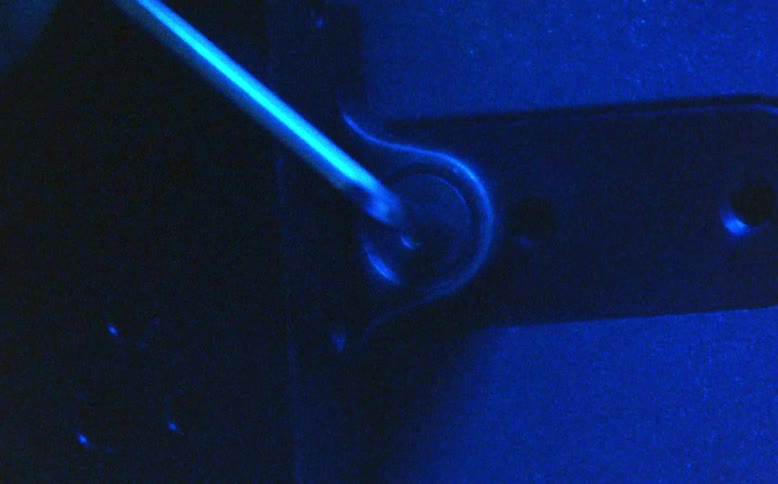A tense, grainy close-up shows a lock being picked with a tool under shifting red, green, and blue lights