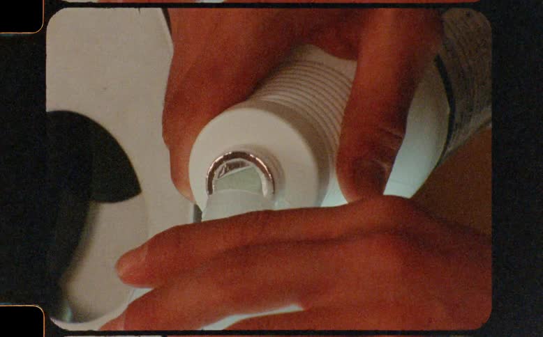 Vintage close-up of hands pouring a clear liquid from a larger bottle into a smaller plastic container