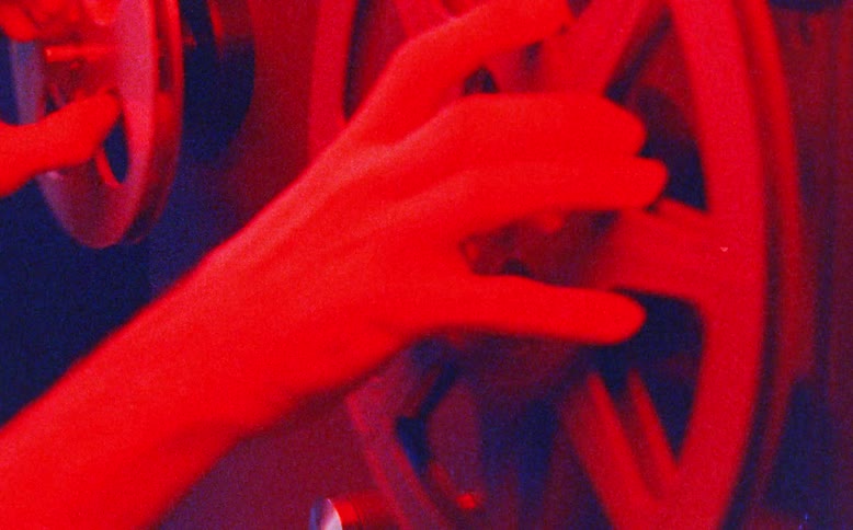 Close-up of hands adjusting the reels of an old film projector in a dark room with dramatic blue and red lighting
