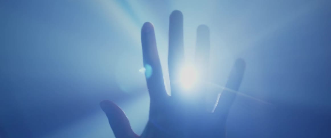 A hand being raised in front of a bright light spreads its fingers