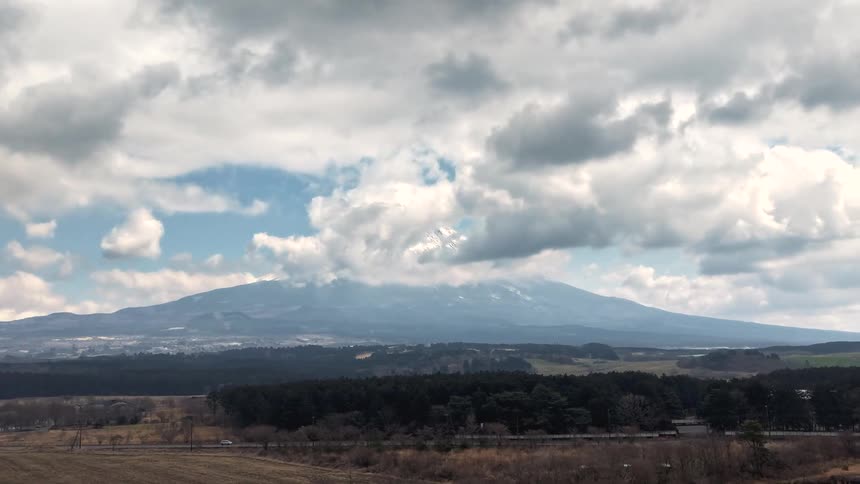 A slow aerial pullback reveals the stunning landscape surrounding Mount Fuji as clouds drift across its snowy peak