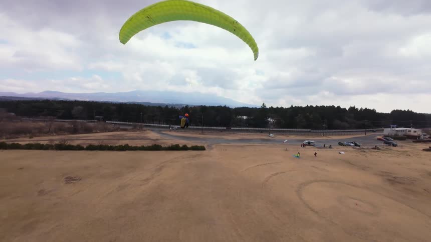 A paraglider soars gracefully over a vast field, executing turns on a cloudy day