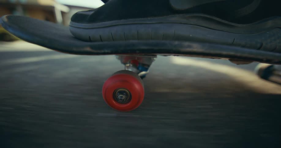 Close-up of a red skateboard wheel spinning on pavement as it glides down the street in the bright sun