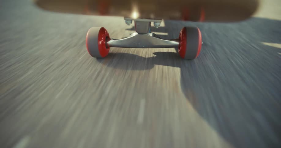 A low-angle, point-of-view shot from the front of a skateboard shows its wheels spinning rapidly as it speeds down a paved road