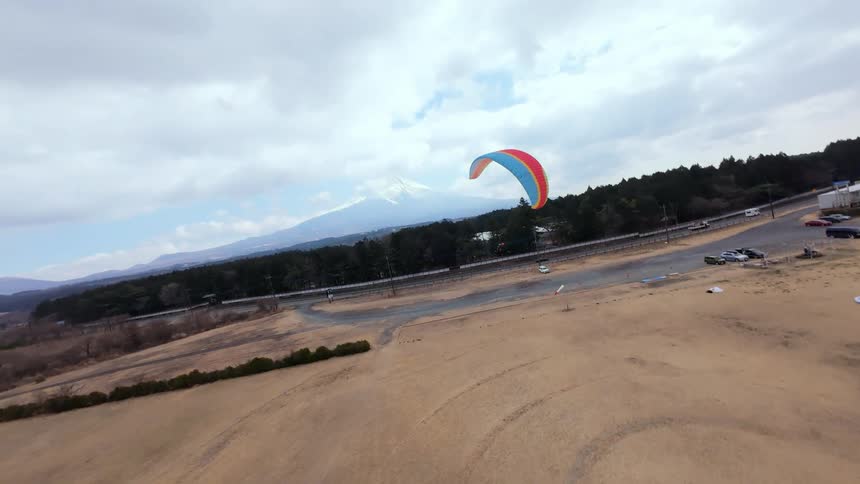 An aerial view follows a colorful paraglider soaring through the sky, revealing the majestic snow-capped Mount Fuji in the background