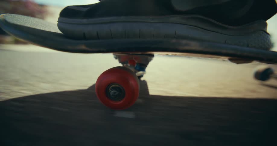 A cinematic low-angle close-up of a red skateboard wheel spinning rapidly as it cruises along the pavement on a bright, sunny day