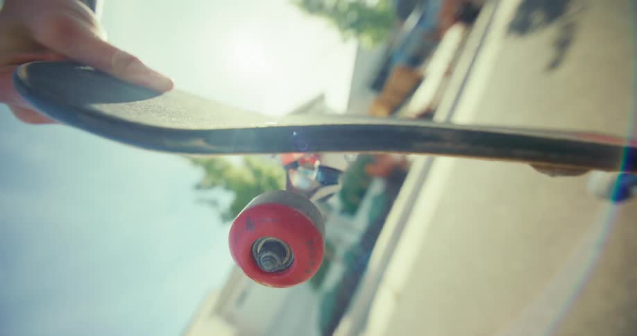 Point of view of a skateboard as a hand pushes it to roll down a sunny suburban street in slow motion