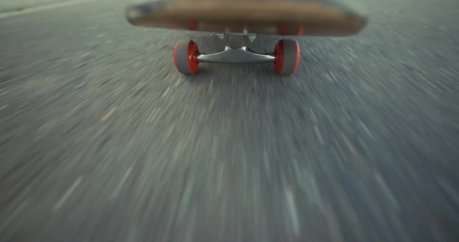 A fast point-of-view shot of a skateboard cruising down a paved road on a sunny day