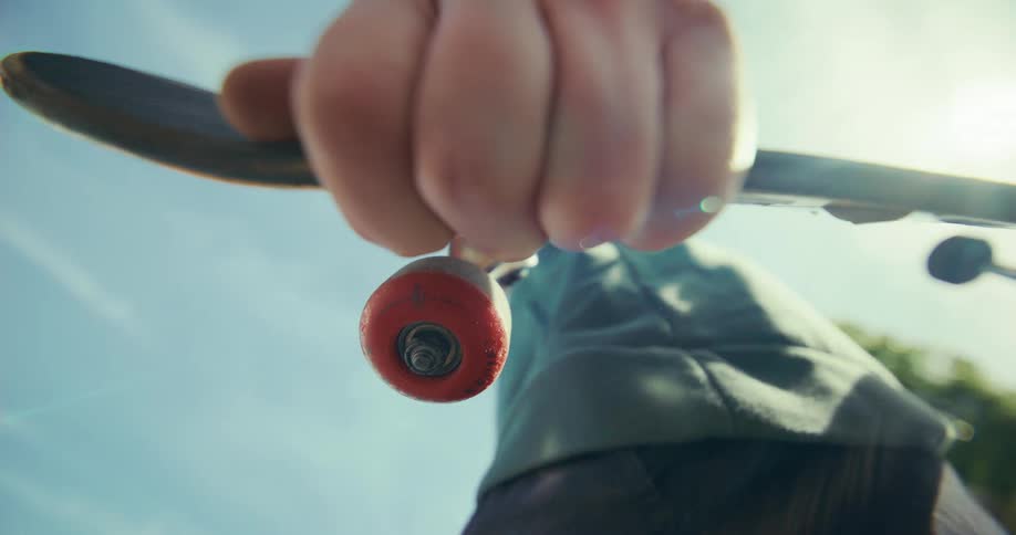 Low-angle close-up of a person holding a skateboard with a red wheel against a sunny blue sky