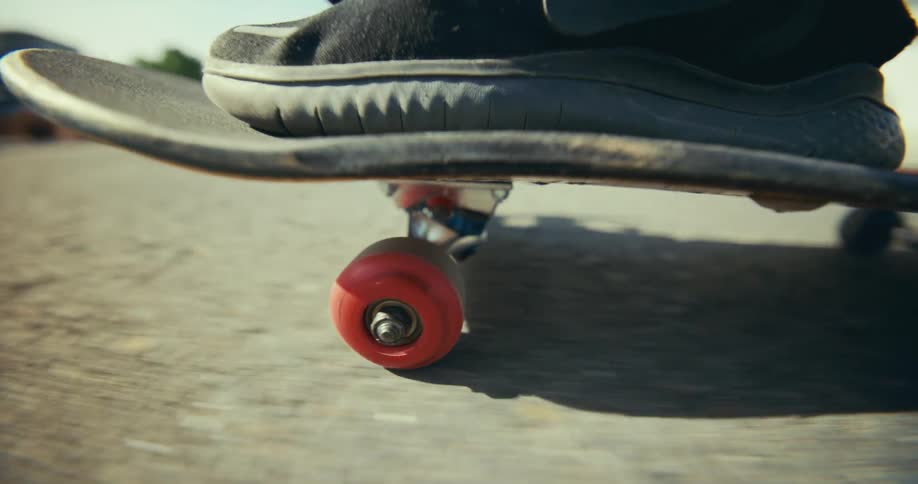 A macro shot captures the red wheel of a skateboard spinning rapidly as it glides over the pavement