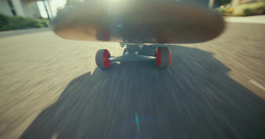 A dynamic low-angle point-of-view shot of a skateboard speeding down a sunny suburban street