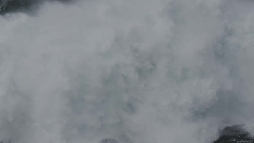 A massive, powerful ocean wave crests and crashes in dramatic slow motion, creating a wall of white water spray