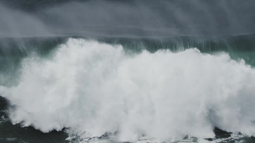 A massive dark ocean wave crests and crashes in dramatic super slow motion, viewed from directly above