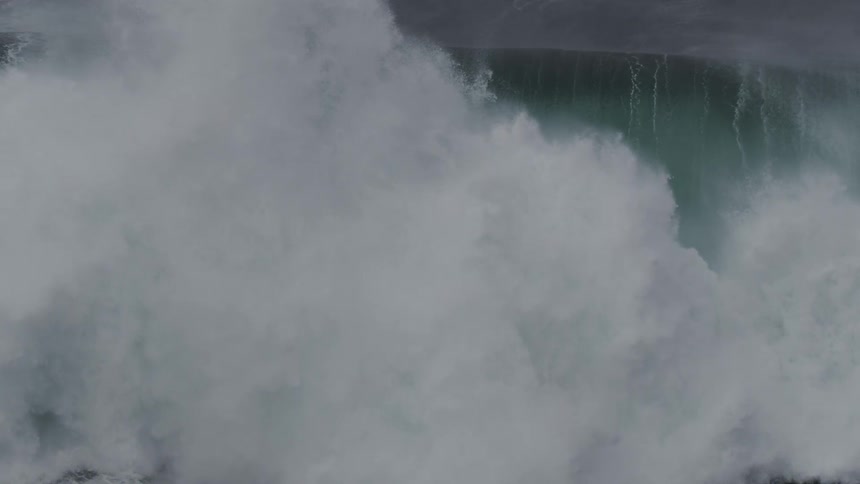 A massive, dark ocean wave crests and crashes in a powerful display of nature's force, captured in stunning super slow motion