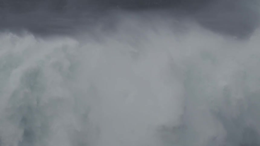 A massive dark ocean wave crashes in dramatic ultra-slow motion, filling the frame with turbulent white water