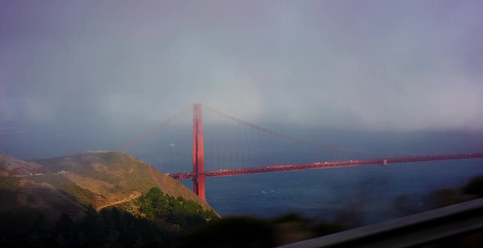 A passenger's view from a moving car captures the iconic Golden Gate Bridge shrouded in heavy fog