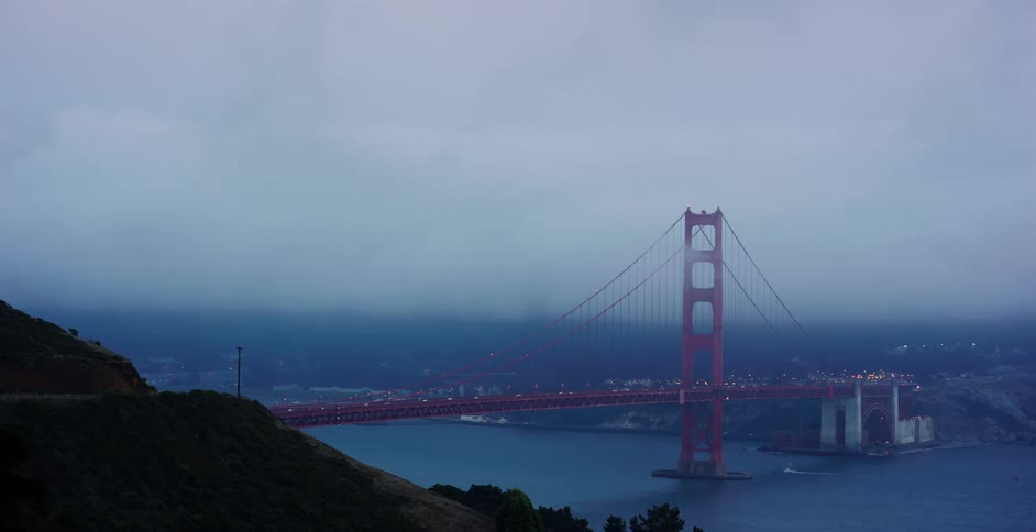 The iconic Golden Gate Bridge stands shrouded in thick fog at dusk as traffic flows across its expanse