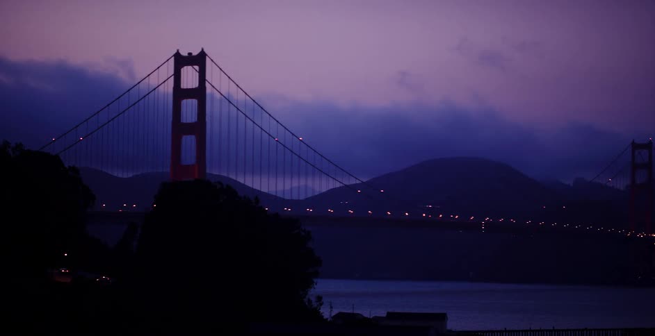 A silhouetted view of the Golden Gate Bridge at dusk as the camera slowly reveals the iconic landmark under a purple sky