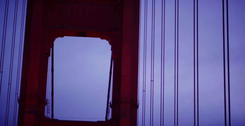 A detailed slow-panning shot captures the iconic red tower and suspension cables of the Golden Gate Bridge against a purple twilight sky