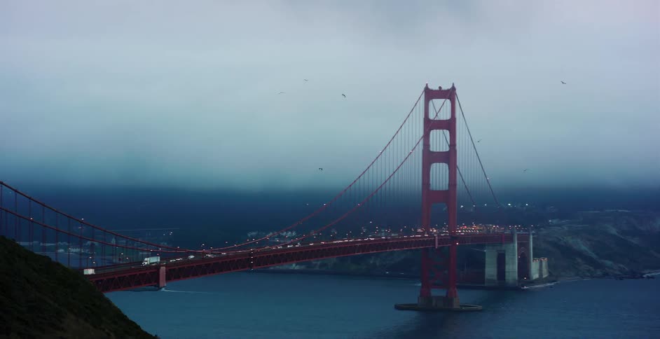 A moody wide shot of traffic crossing the iconic Golden Gate Bridge in San Francisco on a foggy, overcast evening