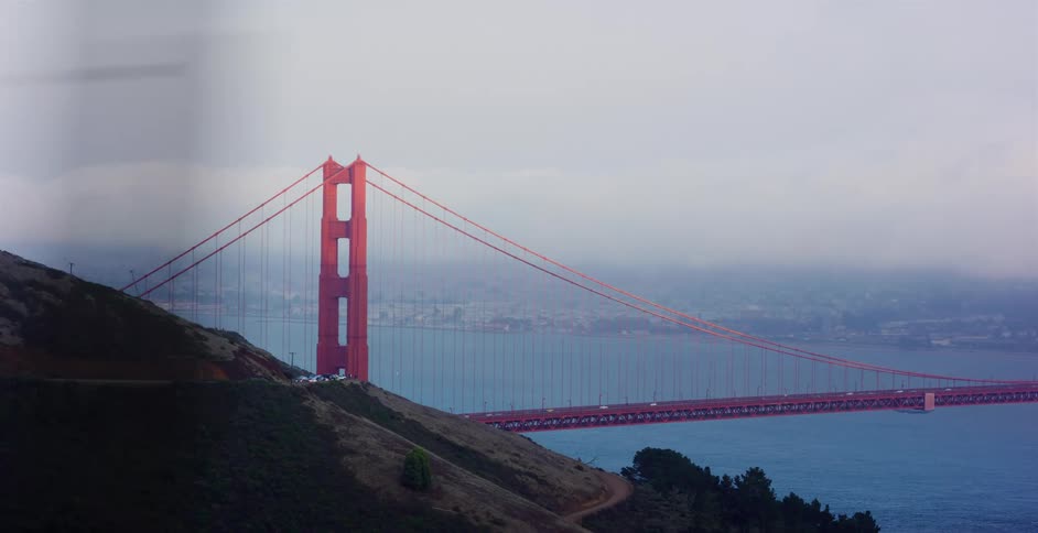 An atmospheric view of the iconic Golden Gate Bridge with traffic crossing on a foggy day from a hillside vantage point