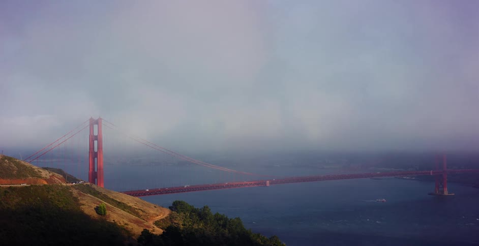 A scenic drive past the iconic Golden Gate Bridge as it stands majestically over the water, partially shrouded in thick morning fog