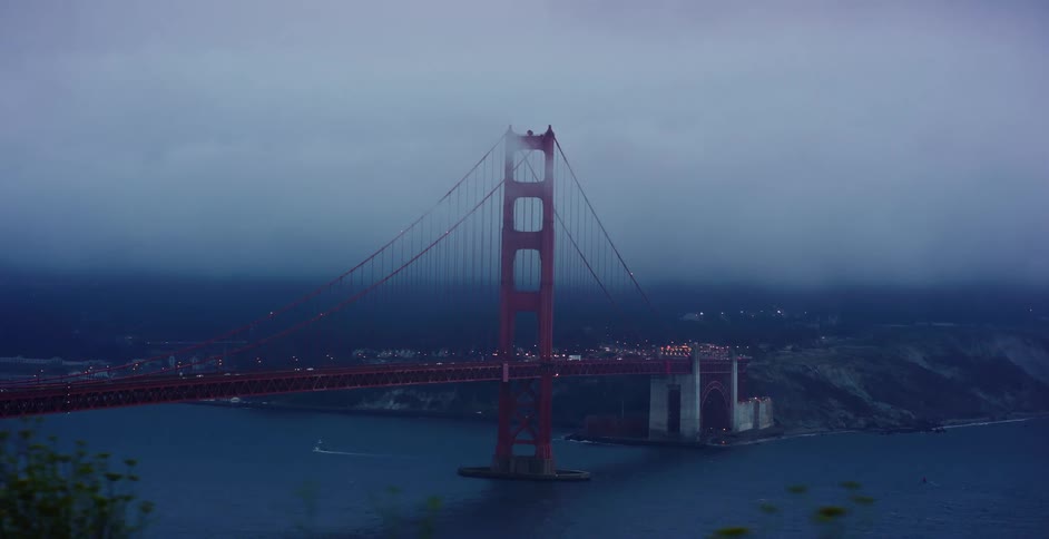 A dramatic wide shot of the iconic Golden Gate Bridge in San Francisco as traffic flows under heavy, moody fog at twilight