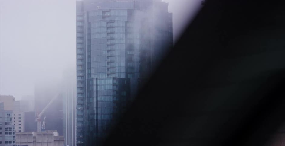 A moving perspective reveals a view of towering modern skyscrapers shrouded in dense fog on an overcast day