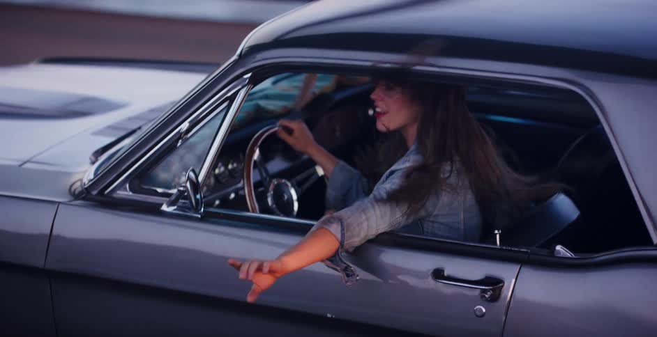 A carefree woman with her arm out the window enjoys a ride in a classic car, her hair blowing in the wind in slow motion