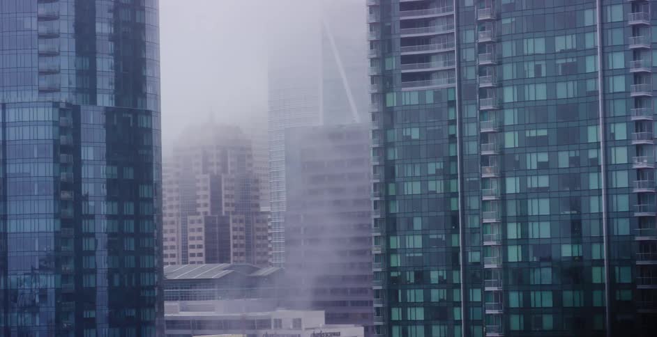 A moody and mysterious view of a foggy downtown cityscape as seen from the window of a moving vehicle