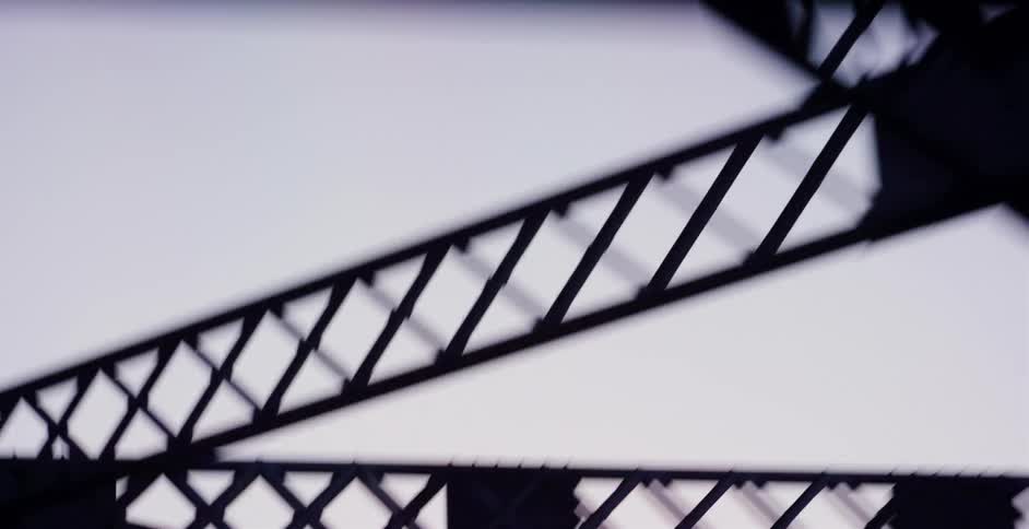 A dizzying, upward-looking perspective of a silhouetted steel truss bridge while driving underneath