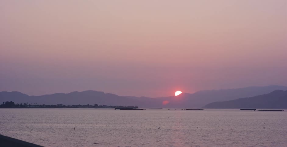 A beautiful purple sunset over a tranquil lake as the sun sinks behind the distant mountains