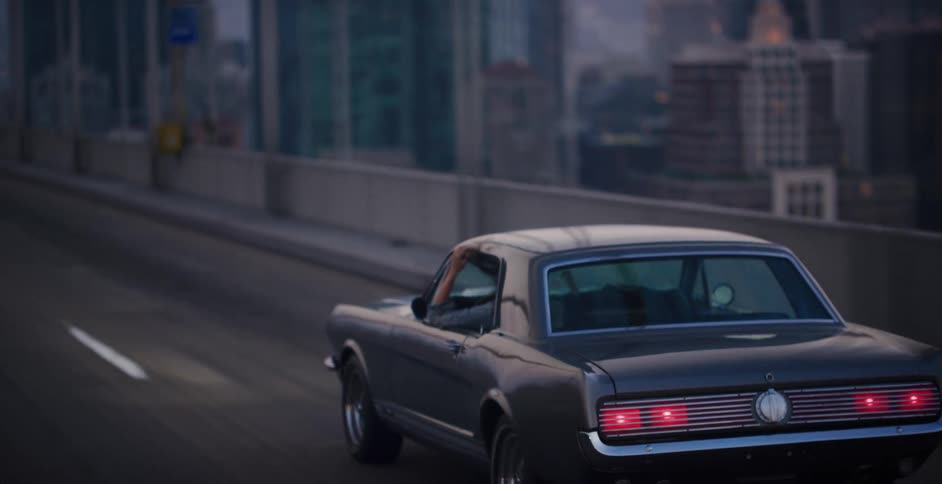 Cinematic slow-motion shot of a vintage grey Ford Mustang driving on a city highway at twilight