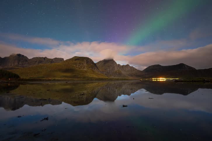 A stunning timelapse of the Northern Lights and starry sky moving above a mountain range, all perfectly reflected in a calm lake