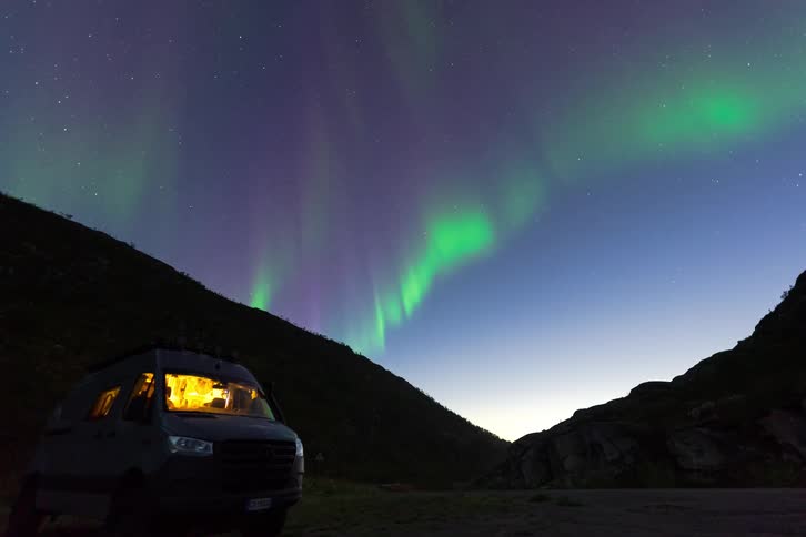 Time-lapse of the colorful Aurora Borealis dancing across the starry night sky above a cozy camper van parked in a remote valley