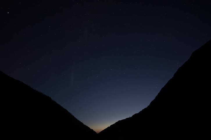 Time-lapse of the vibrant green Aurora Borealis dancing in the starry night sky between two silhouetted mountains