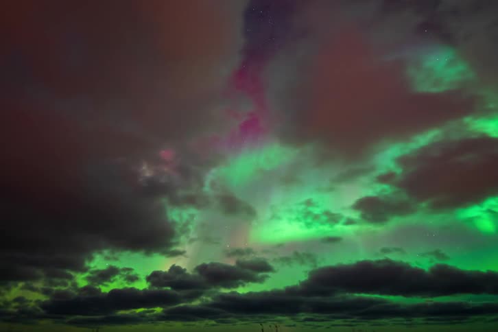 Vibrant green and pink aurora borealis dance across a starry night sky in a dramatic time-lapse with moving clouds