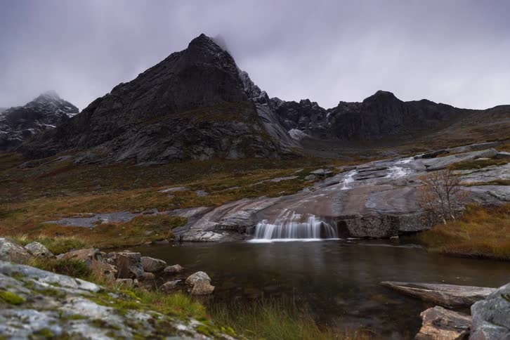A stunning dolly shot timelapse reveals a majestic mountain and a serene waterfall on a cloudy autumn day