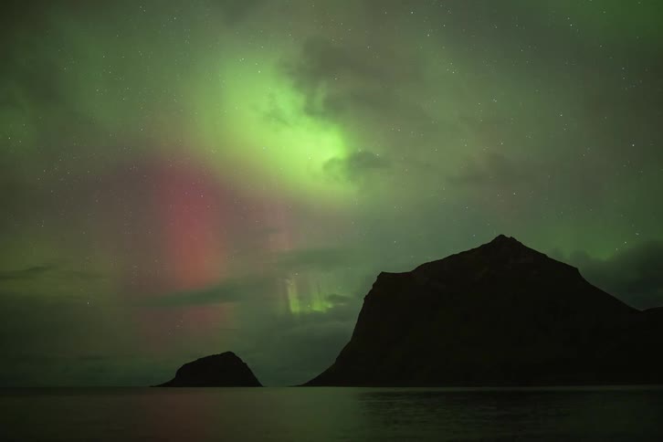 A stunning time-lapse of the colorful Northern Lights dancing over silhouetted mountains and a calm sea