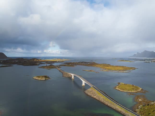 Dramatic aerial pullback reveals a stunning rainbow arching over a scenic bridge that connects a series of remote islands