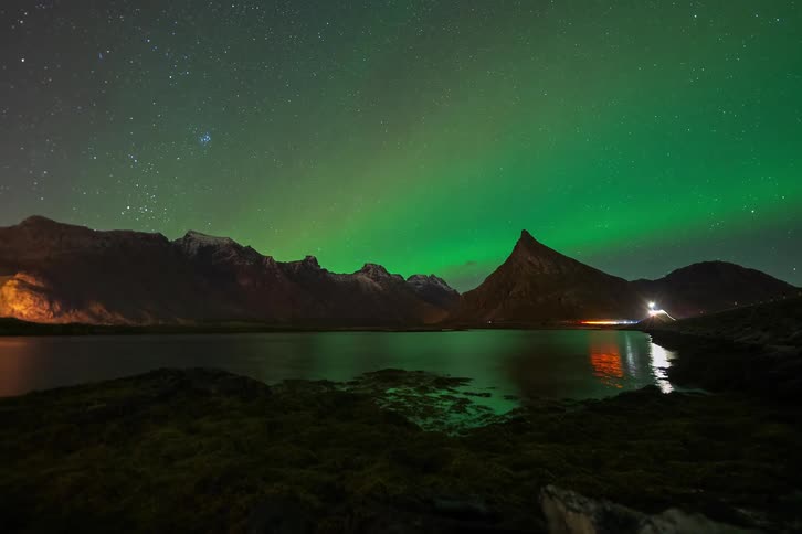 A mesmerizing time-lapse captures the colorful dance of the Aurora Borealis across a starry night sky, reflecting over a calm mountain lake