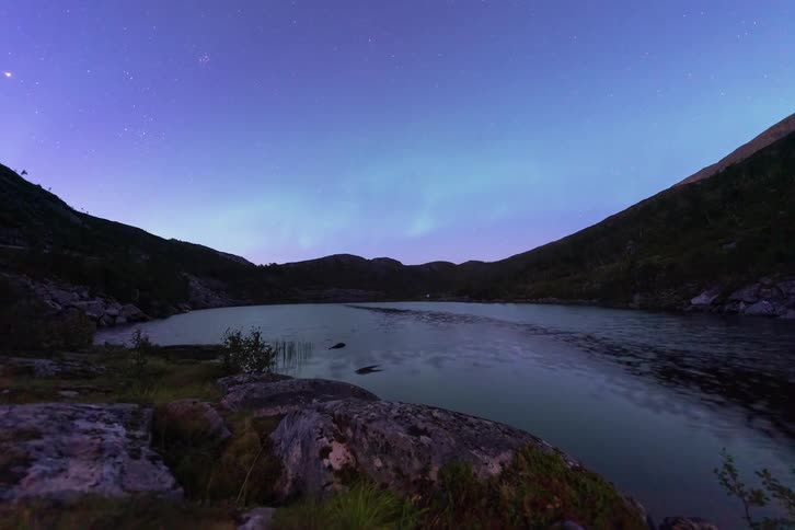 A stunning time-lapse dolly shot of the Aurora Borealis dancing in the starry sky over a tranquil mountain lake