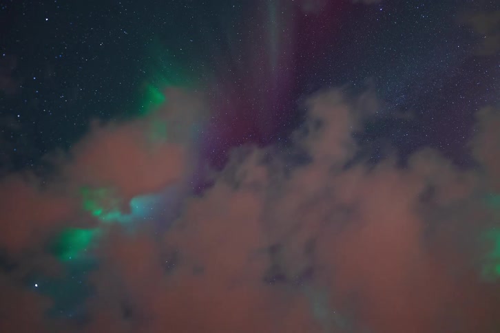 A celestial time-lapse of the vibrant green and purple Aurora Borealis dancing across the starry night sky through moving clouds