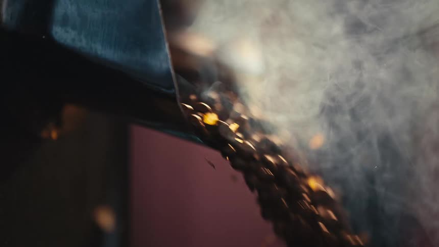 Slow motion close up of fragrant, steaming coffee beans being released from a roaster